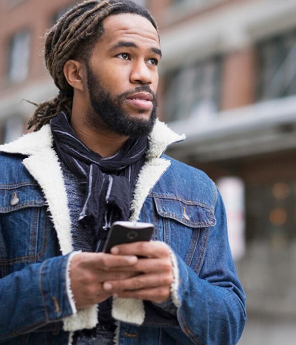 A man with dreadlocks is using his mobile phone to report something he's seen happening on the street.