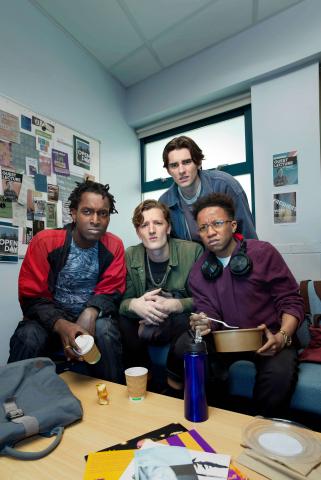 Four male students in a university classroom, looking to camera with disgusted expressions.