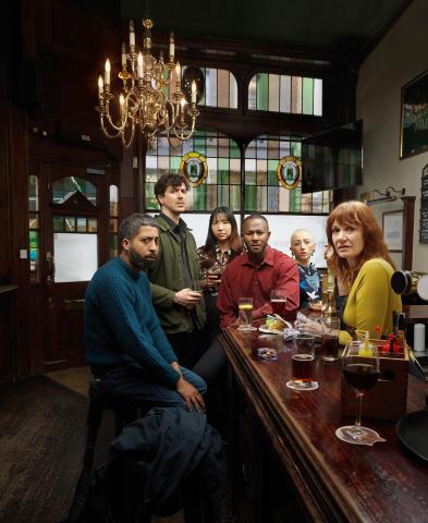 Group of people in a bar looking to camera with concerned expressions. 